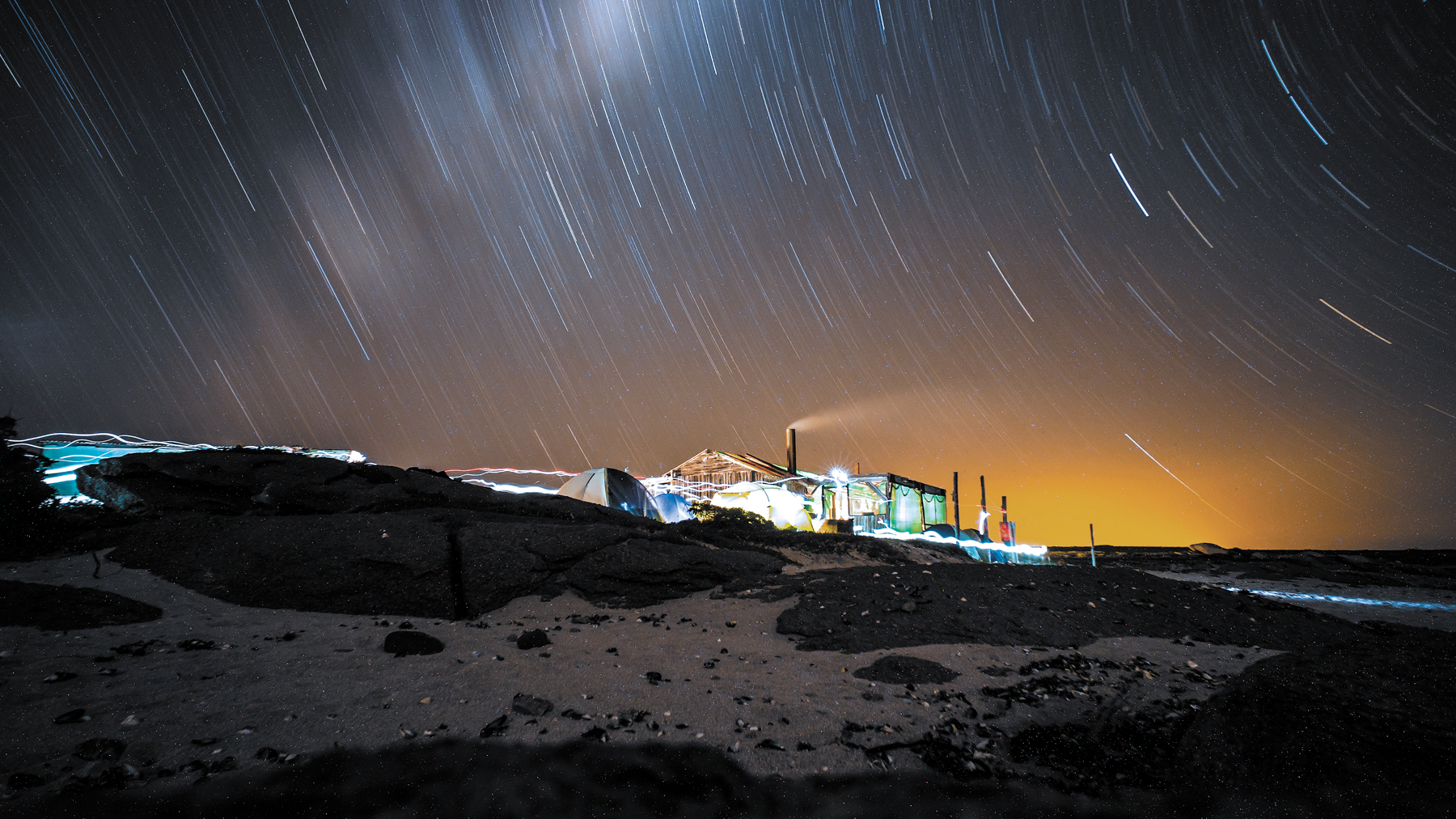After image shows tents on a beach at night with orange hues corrected and blue tones added to the sky.