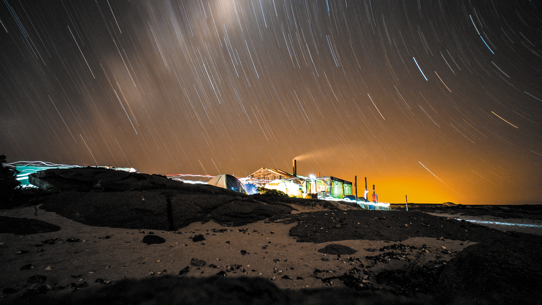 Before image shows tents on a beach at night with orange-hued sky.